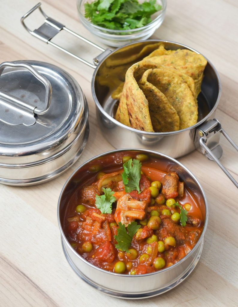 Indisches Pilz-Curry mit Erbsen und Roti (Fladenbrot) in einer Lunchbox (Tiffin-Box)