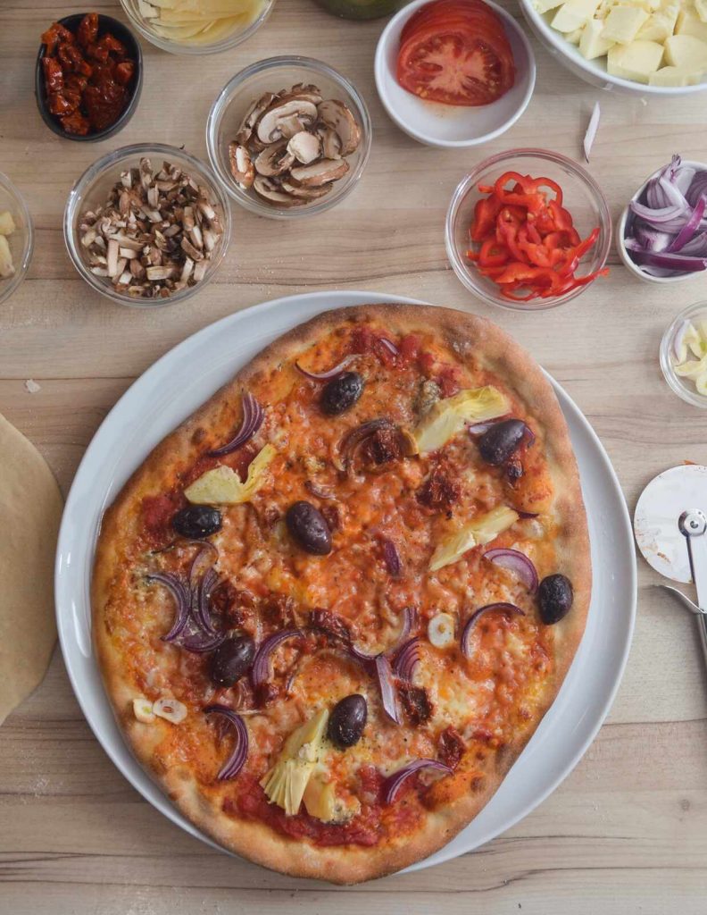 Selbstgemachte Pizza mit Oliven, Artischocken und Zwiebeln