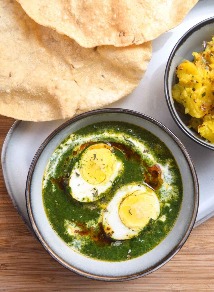 Palak Anda Curry, indisches Spinat-Curry mit Eiern. Daneben Jira Aloo und Papadums